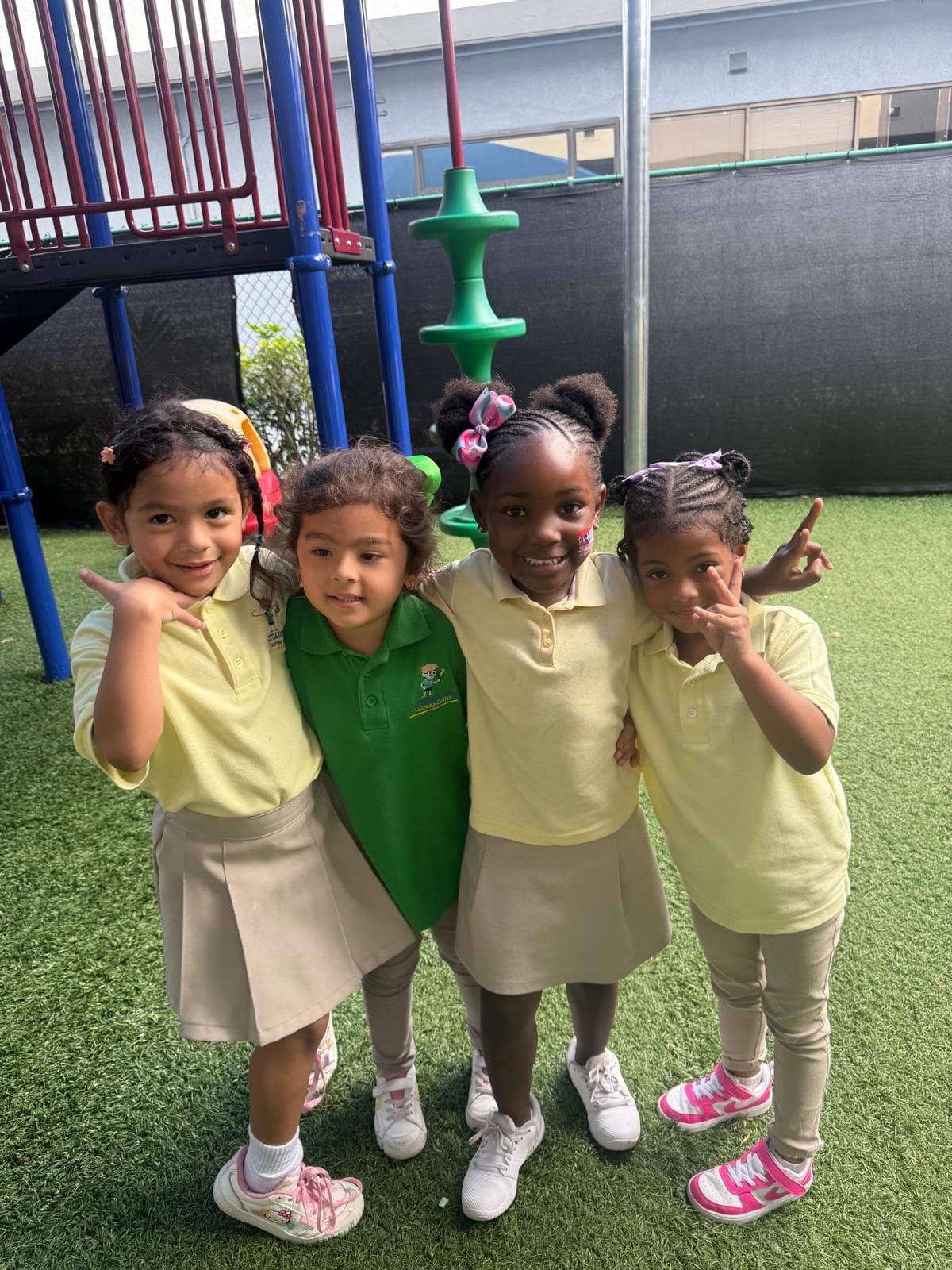 Four children standing together on an outdoor playground with their arms around each other