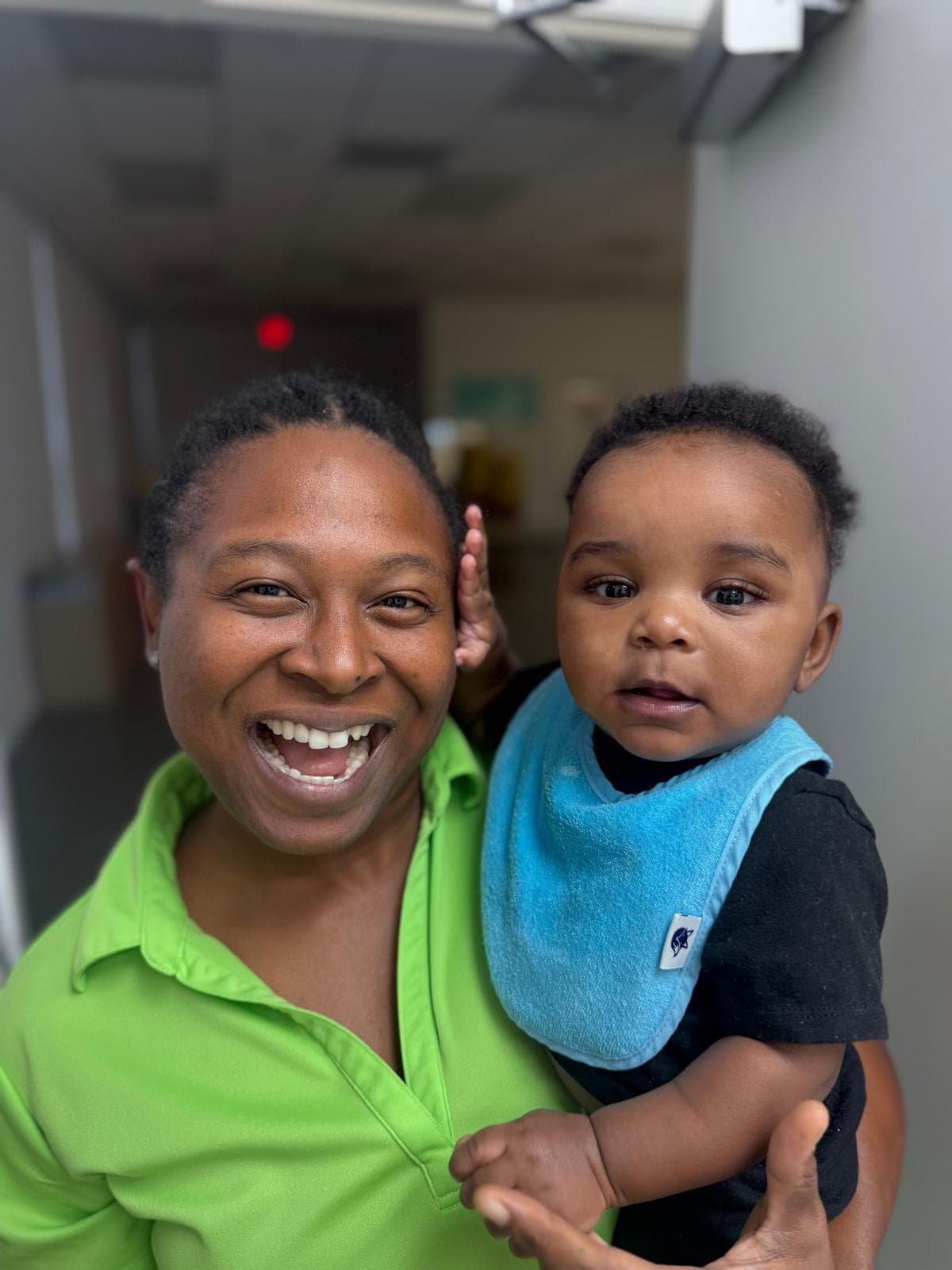 A caregiver smiling while holding an infant in a hallway