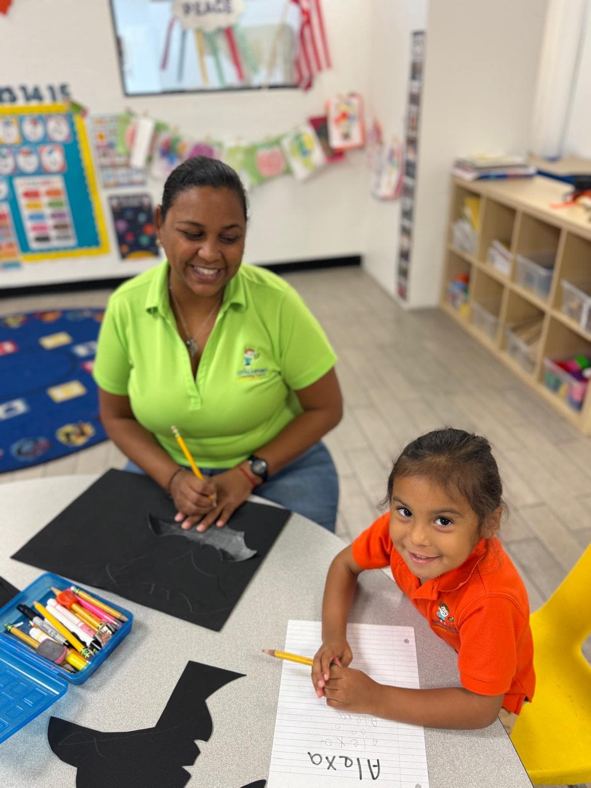 A teacher and a child seated at a table working on a craft activity in a classroom