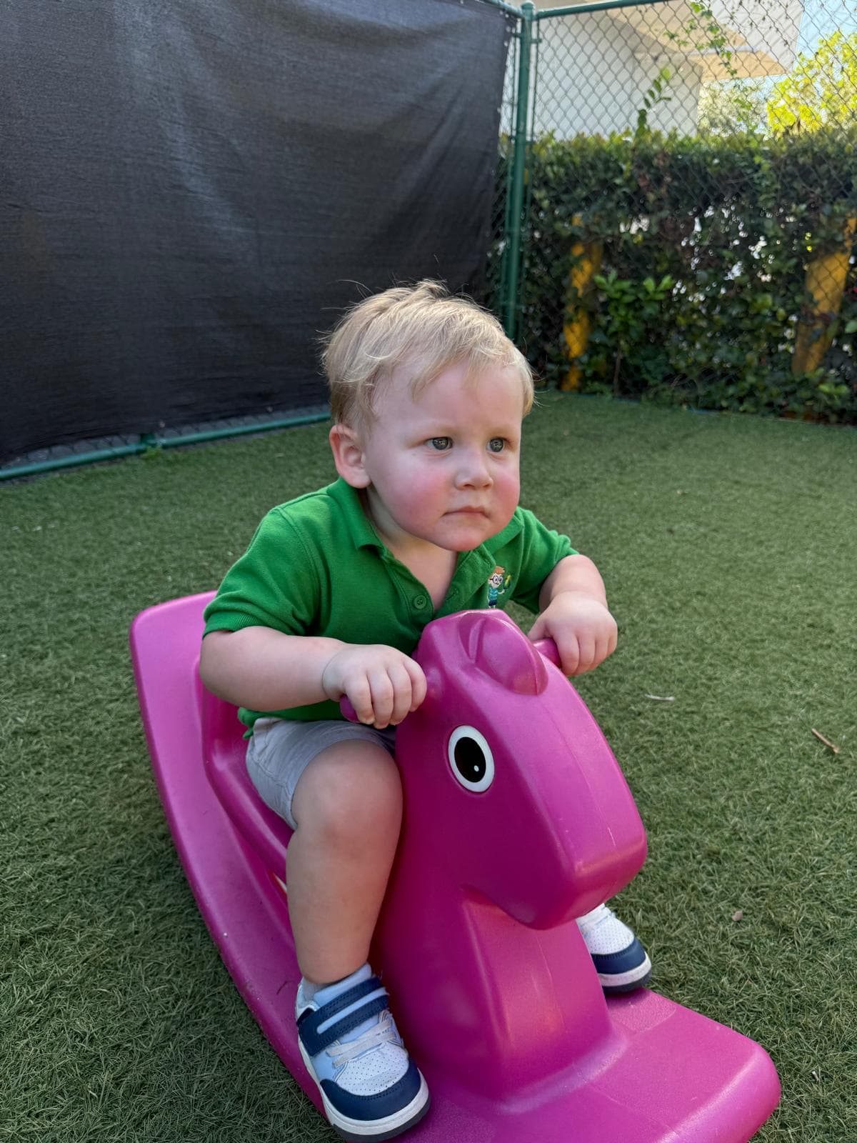 A toddler in a green polo shirt riding a rocking-horse toy outdoors